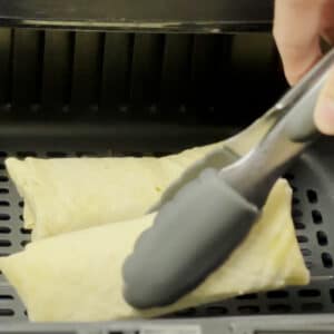 Putting the frozen burrito in air fryer using tongs